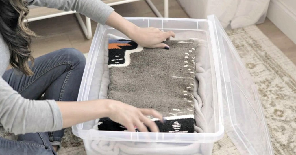 woman adding folded sweaters to a large storage tote