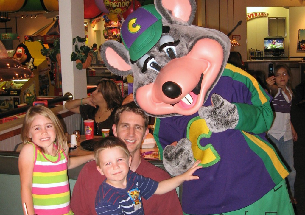 family sitting next to mouse at Chuck E. Cheese