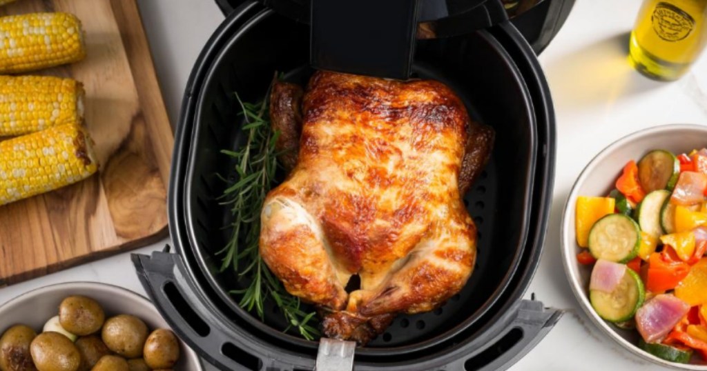 air fryer with a whole chicken in it surrounded by food