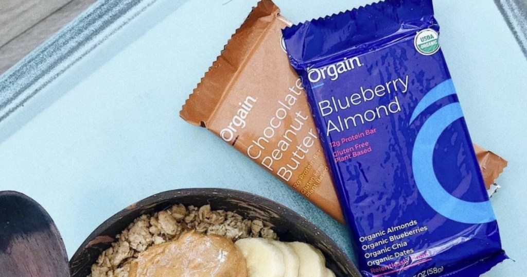 Two flavors of protein bars from Orgain on a counter top with oatmeal bowl
