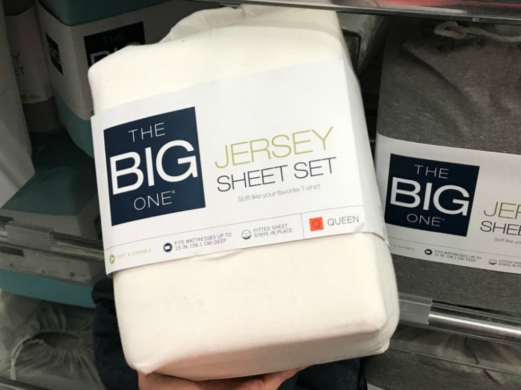 hand holding set of cream colored sheets by store shelf