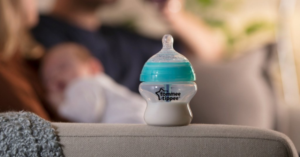 Tommee Tippee Bottle on arm of couch with parents and baby in background