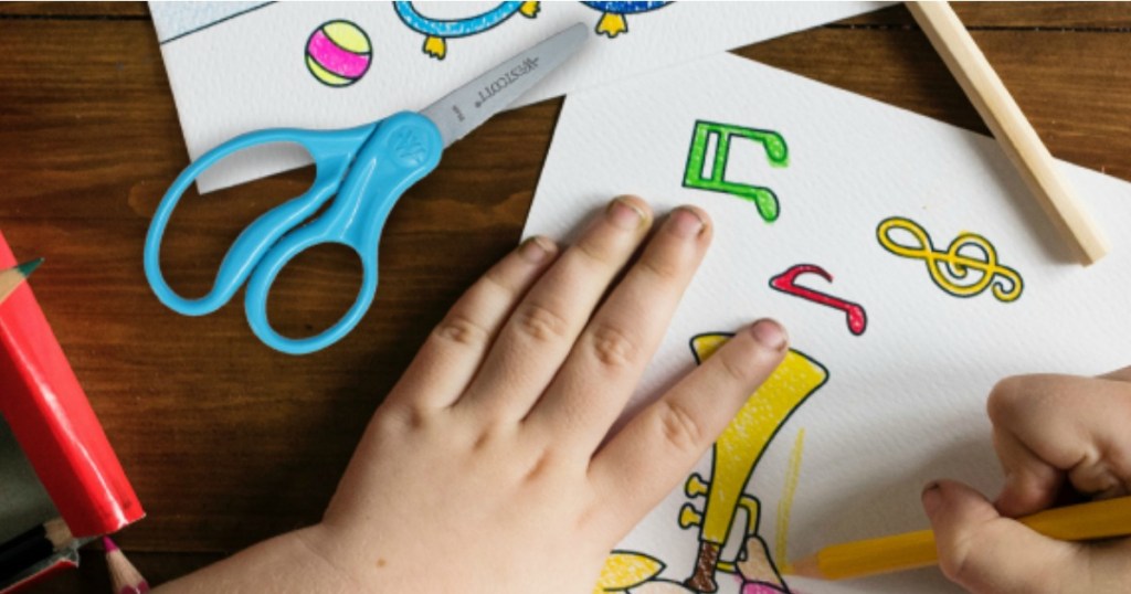 Boy drawing and coloring with pair of scissors next to him
