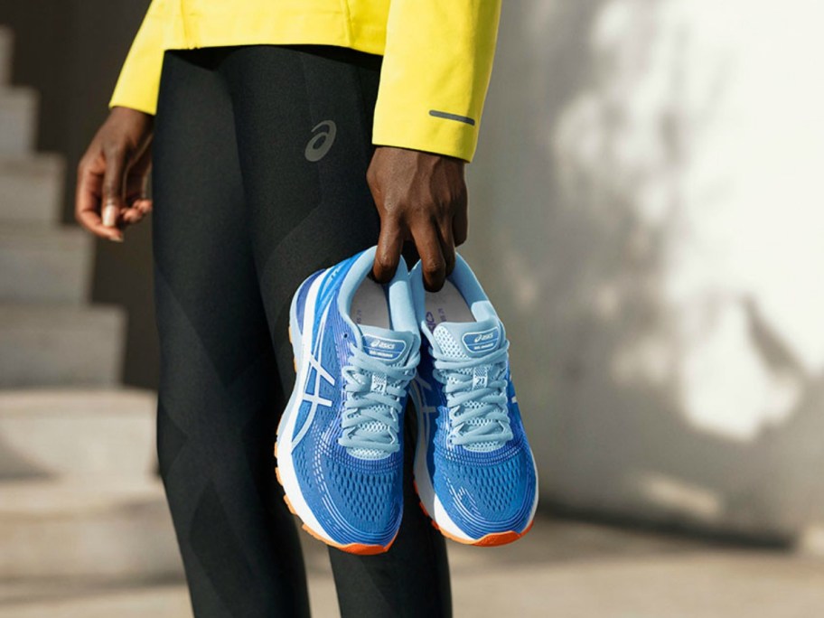 A person holding a pair of blue ASICS running shoes