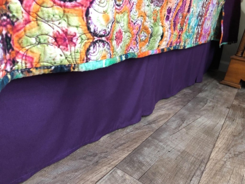 purple bed skirt under floral blanket