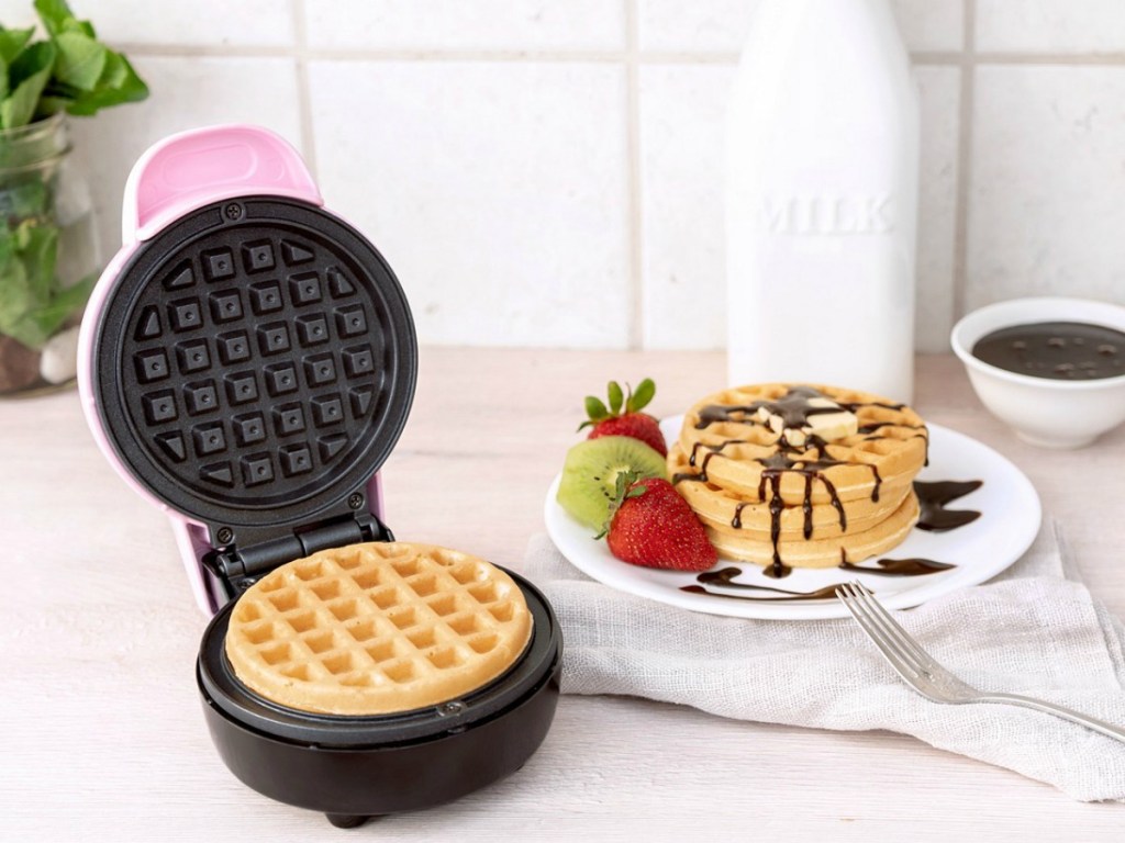 pink waffle maker next to plate of waffles