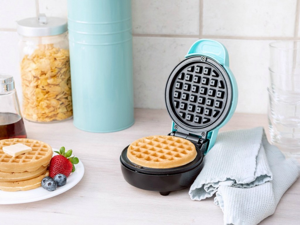 waffle maker on counter next to plate of waffles