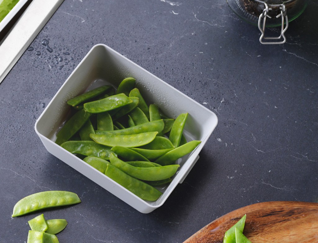 black countertop with bowl of green peas in pod