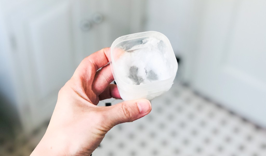 hand holding a small clear tupperware of coconut oil