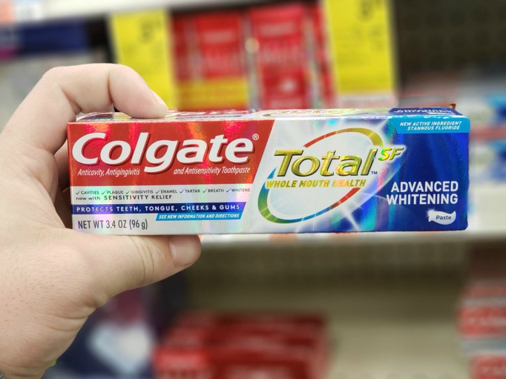 hand holding box of colgate toothpaste by store shelf