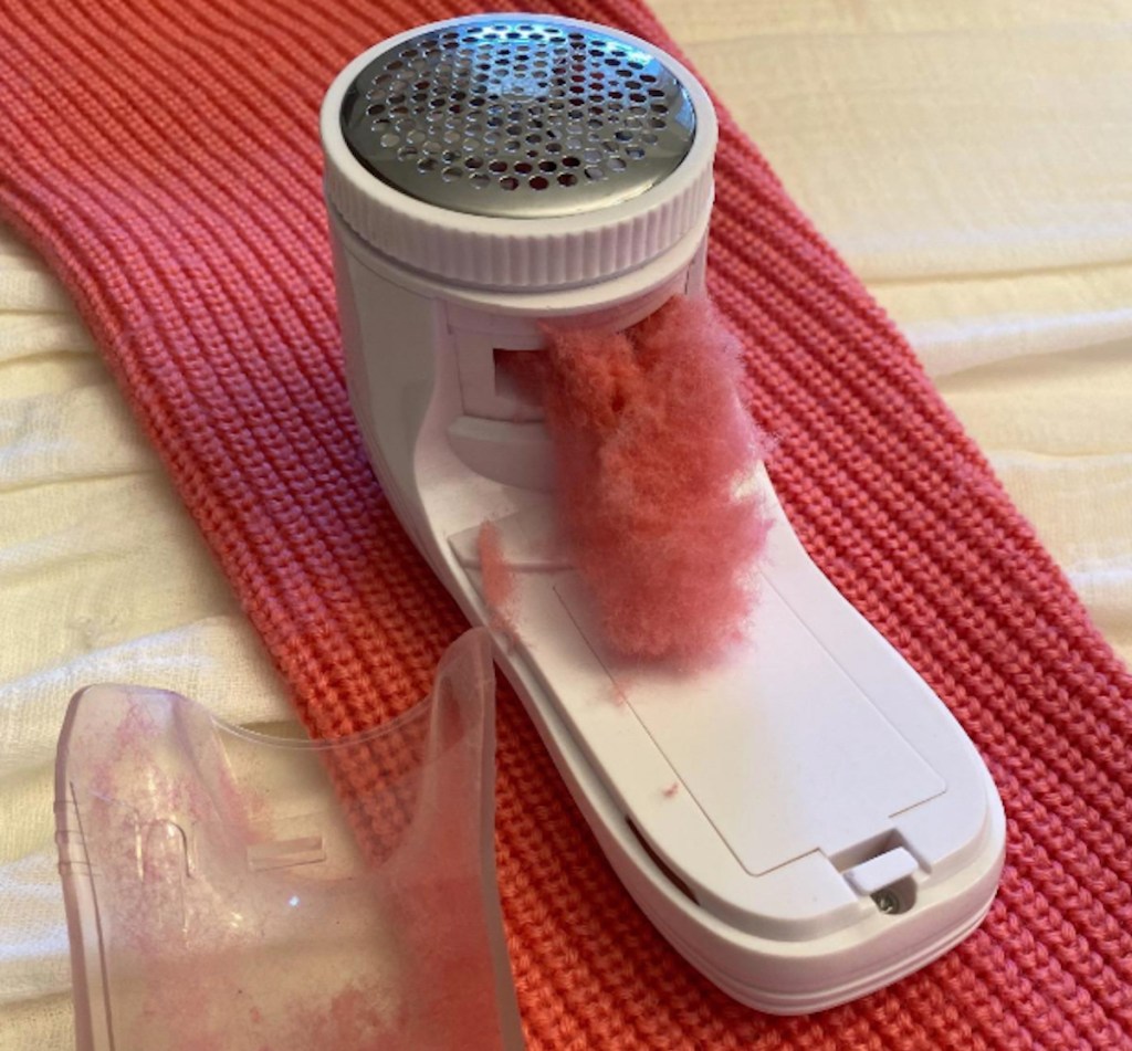 fabric shaver with pink red lint inside sitting on sweater sleeve