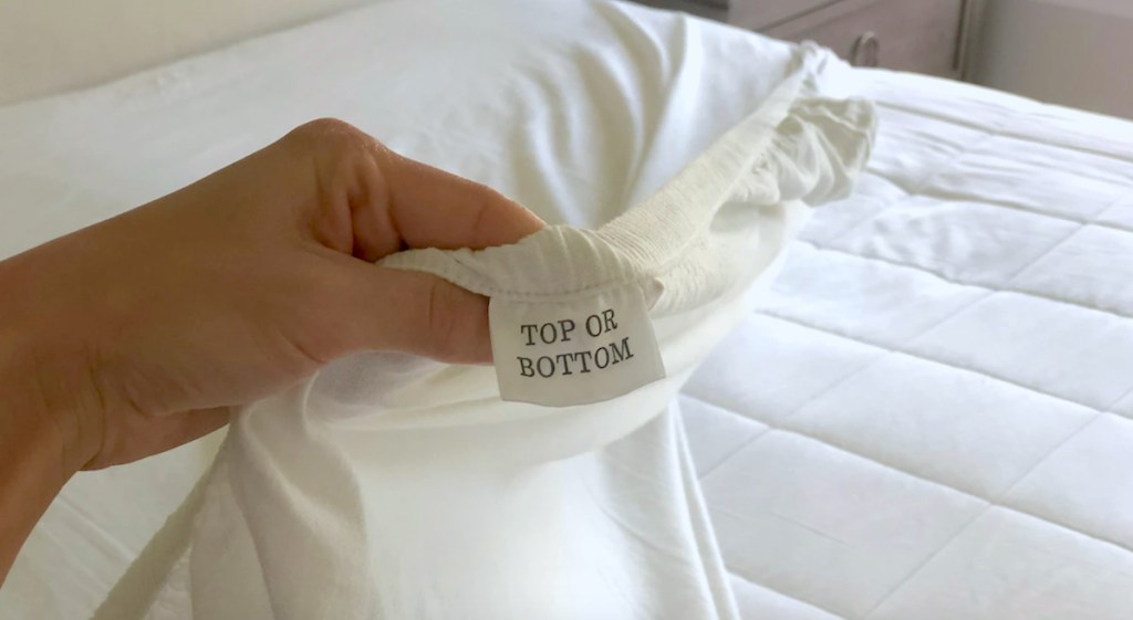 hand holding a fitted sheet with top or bottom tag 