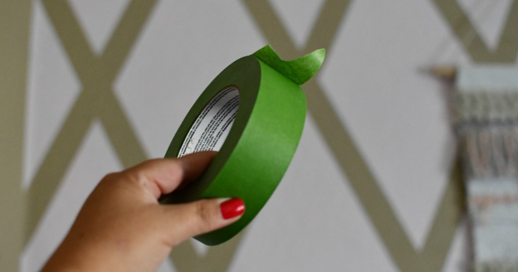 holding green frog tape in front of decorative wall 