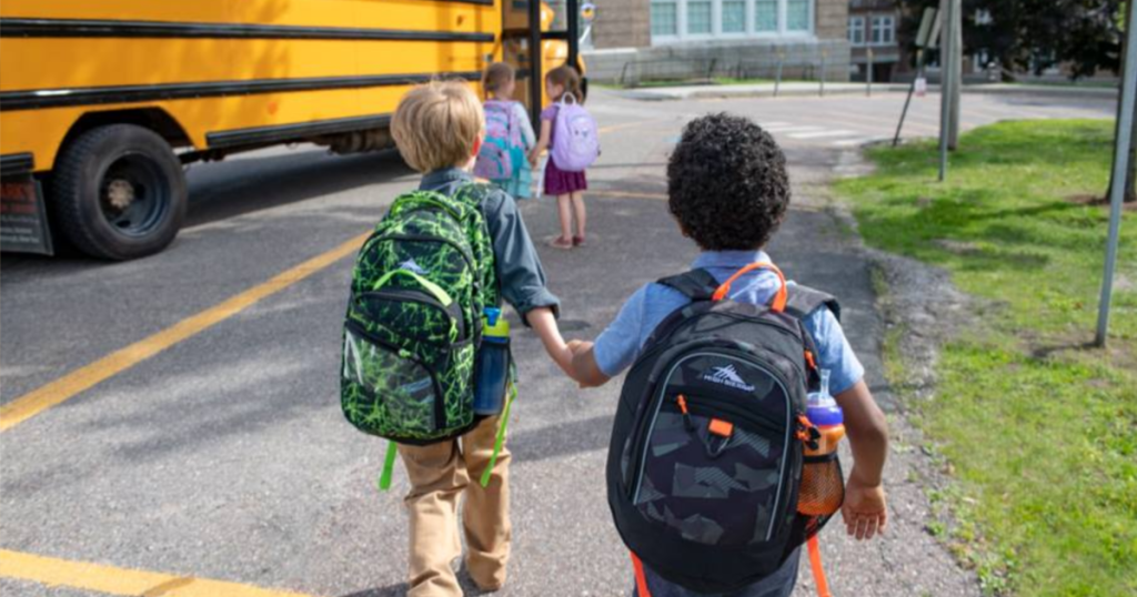 two little kids running toward a yellow school bus wearing backpacks