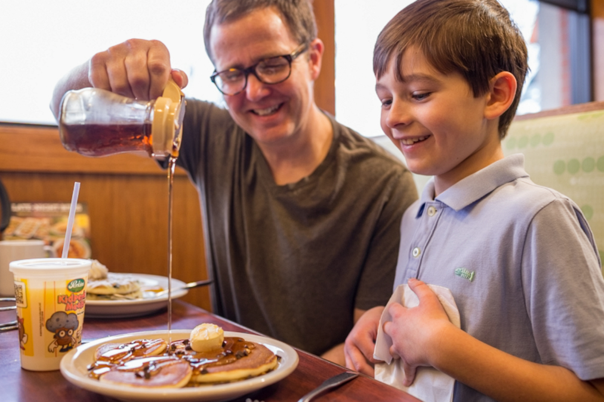 dad pouring syrup on kids pancakes