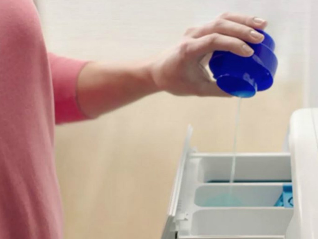 hand pouring laundry soap in washer dispenser
