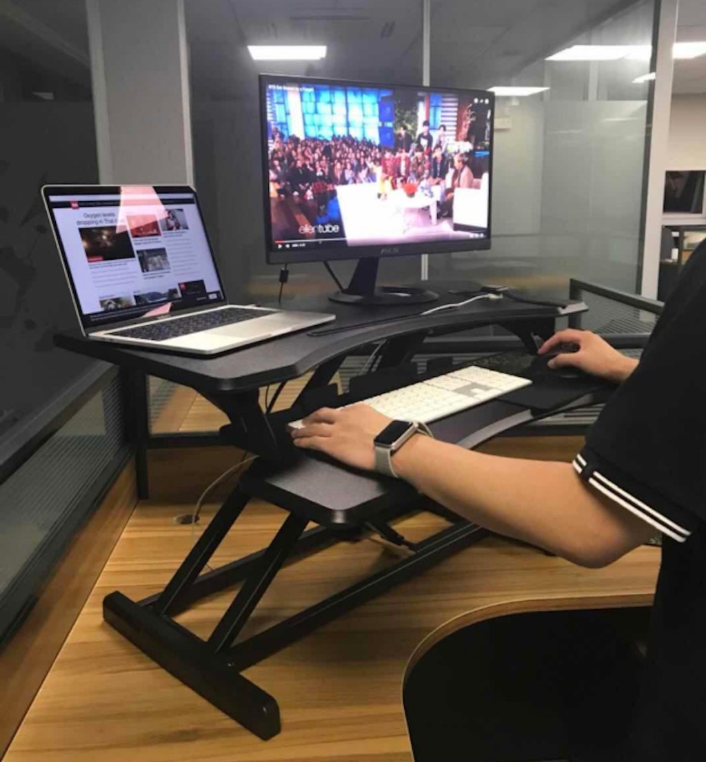 person standing at desk with computer screen and laptop