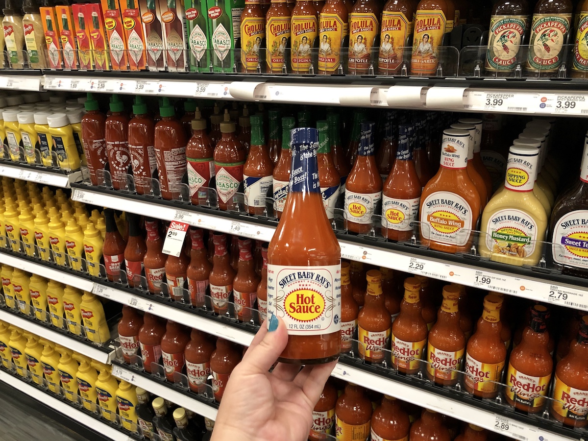 hand holding bottle of Sweet Baby Ray's Hot Sauce in front of store shelf