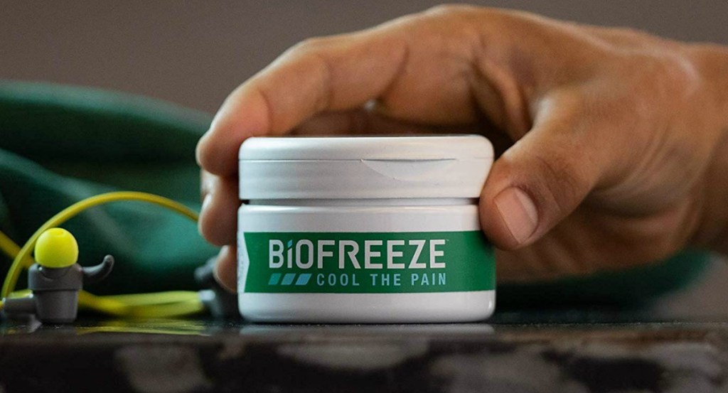 BioFreeze brand pain relief cream in a jar in hand near earbuds