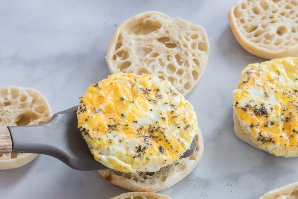 cooked egg being placed on an English muffin