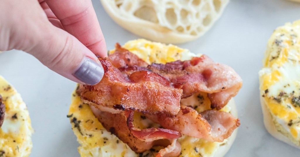 Woman adding bacon to breakfast sandwich