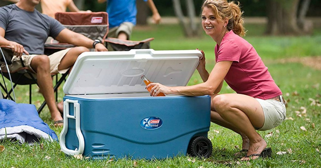 Woman grabbing a bottle out of a blue Coleman cooler outdoors in the grass