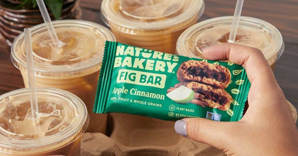 hand holding Nature's Bakery Fig Bar by coffee cups