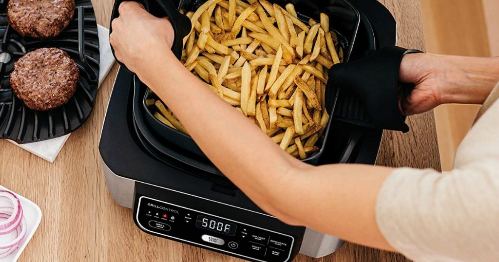 woman lifting the lod on a Ninja Foodi 5-in-1 Grill filled with french fries
