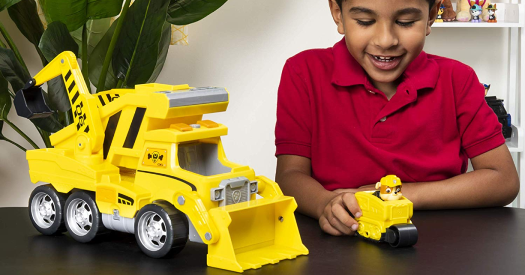Paw Patrol Yellow Rescue Construction Truck with lights and sounds and a mini vehicle on a table with a boy beside it, playing