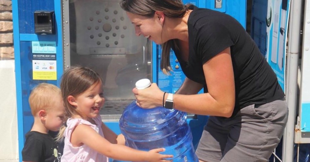 woman handing large water bottle to little girl