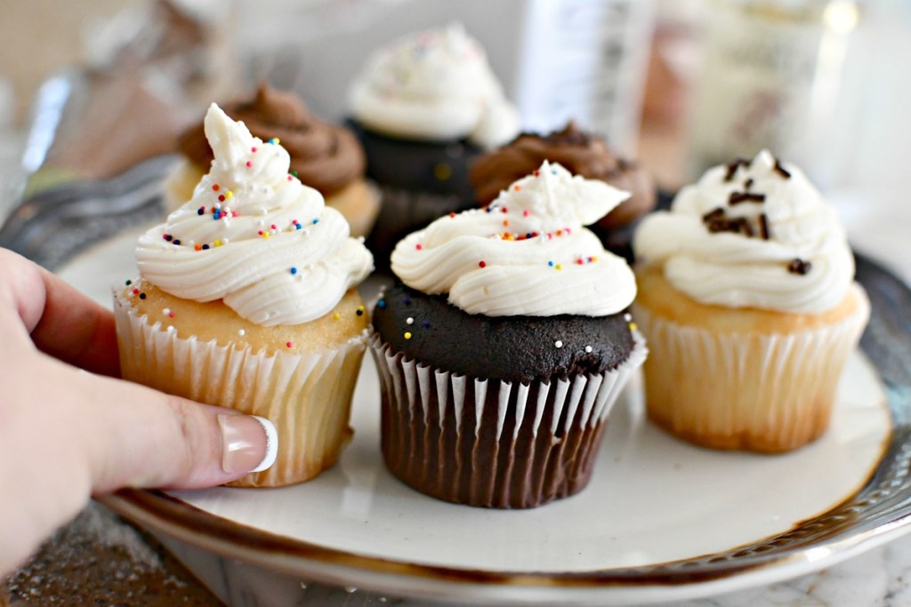 adding buttercream frosting and sprinkles to cupcakes