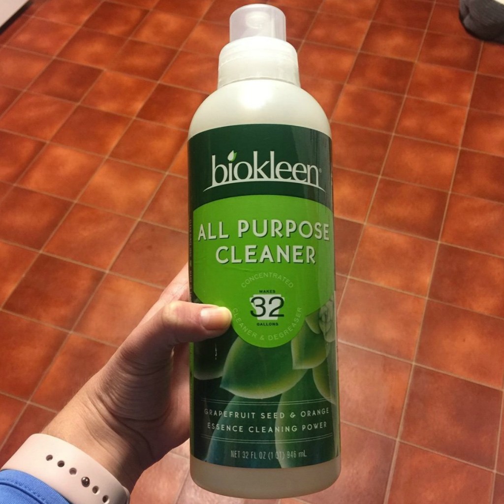Large bottle of biokleen All Purpose Cleaner in hand over hardwood flooring