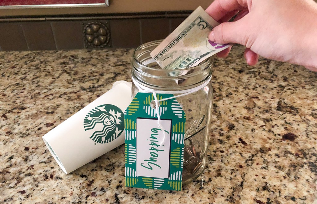 putting $5 bill into money jar next to Starbucks cup