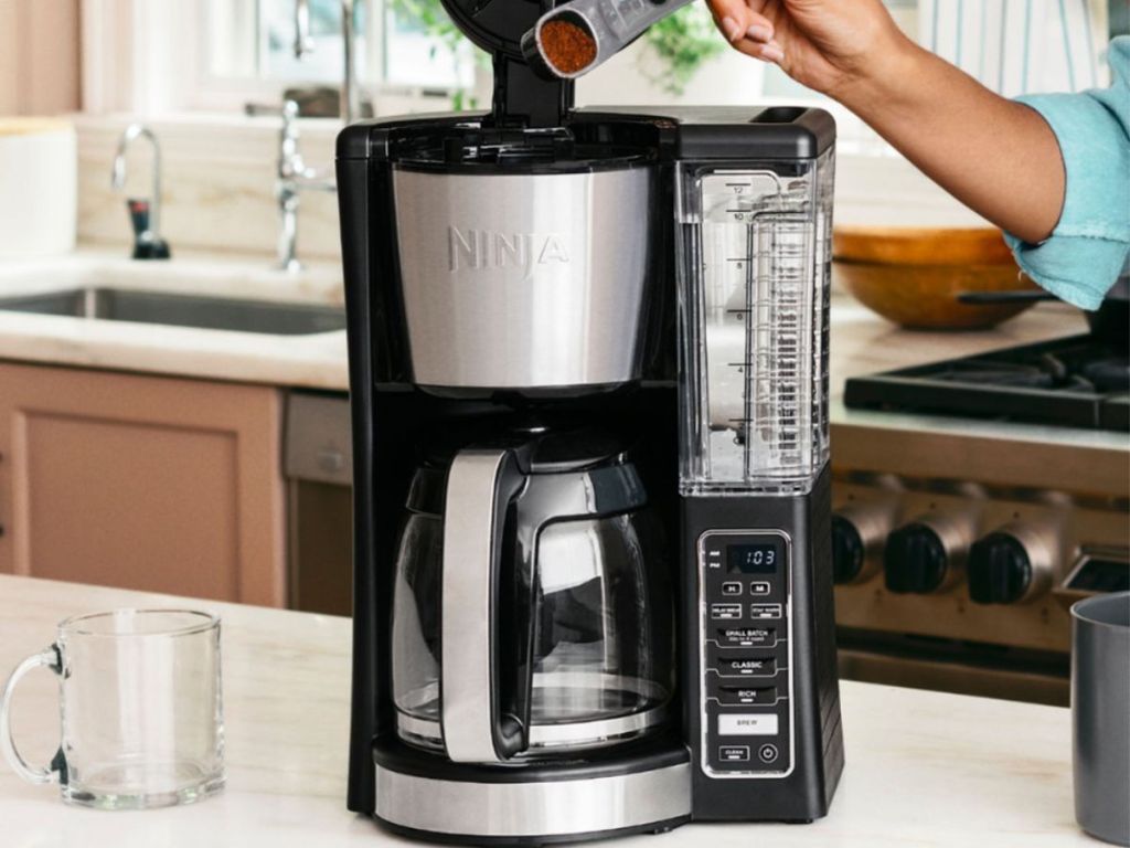 woman putting coffee into ninja coffee maker in kitchen