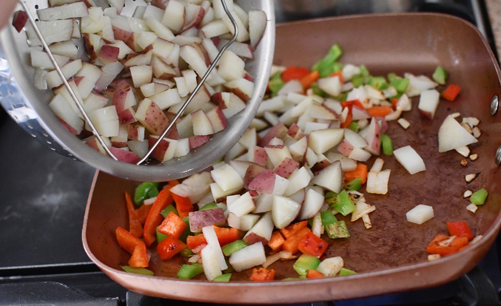 adding potatoes to skillet to make for breakfast burrito pouches