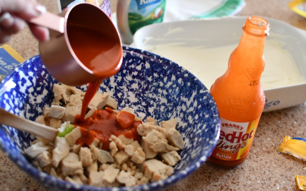 pouring buffalo sauce onto shredded chicken