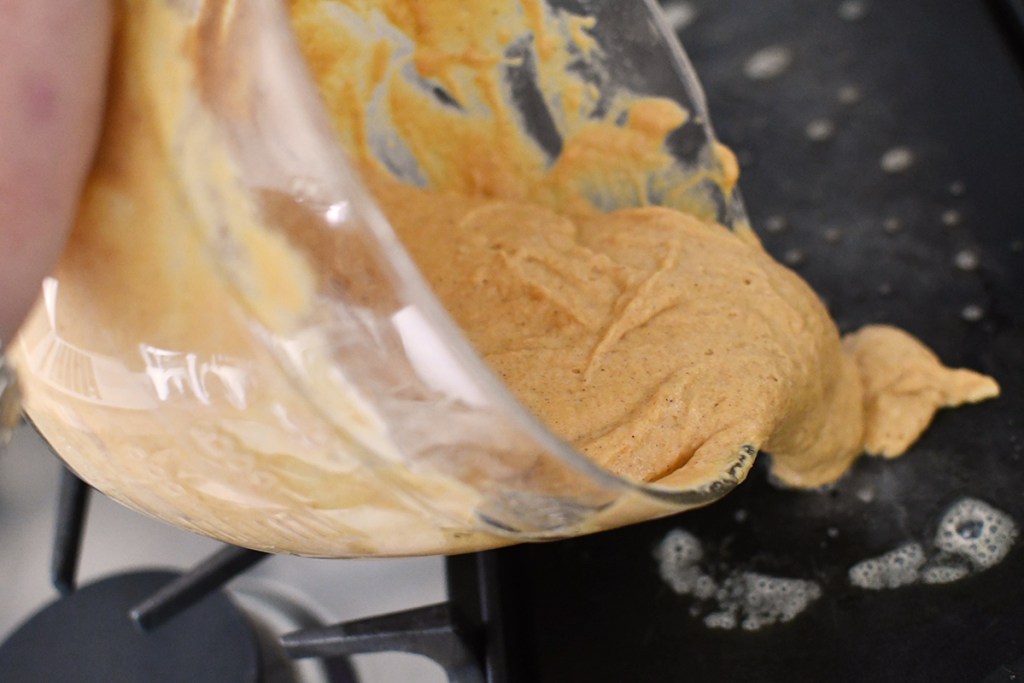 pouring pumpkin pancake battle onto griddle