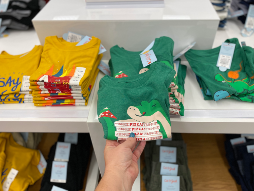 hand holding green tee with other tees on shelf 