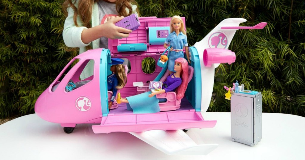 Child playing with a Barbie plane with accessories on a table, outside