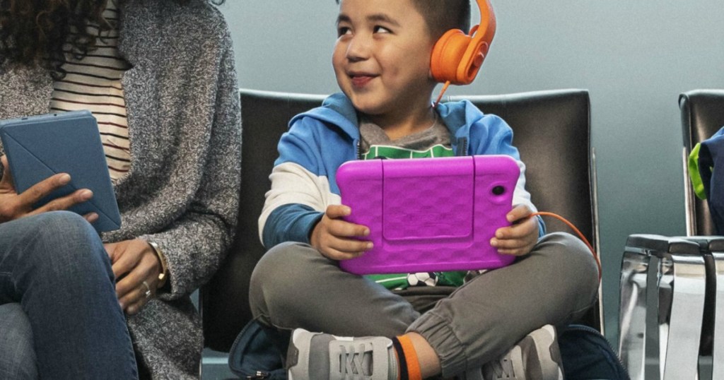Kid sitting next to mom with Fire Tablet, wearing orange headphones 