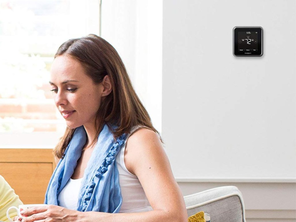 woman sitting on couch with thermostat behind her
