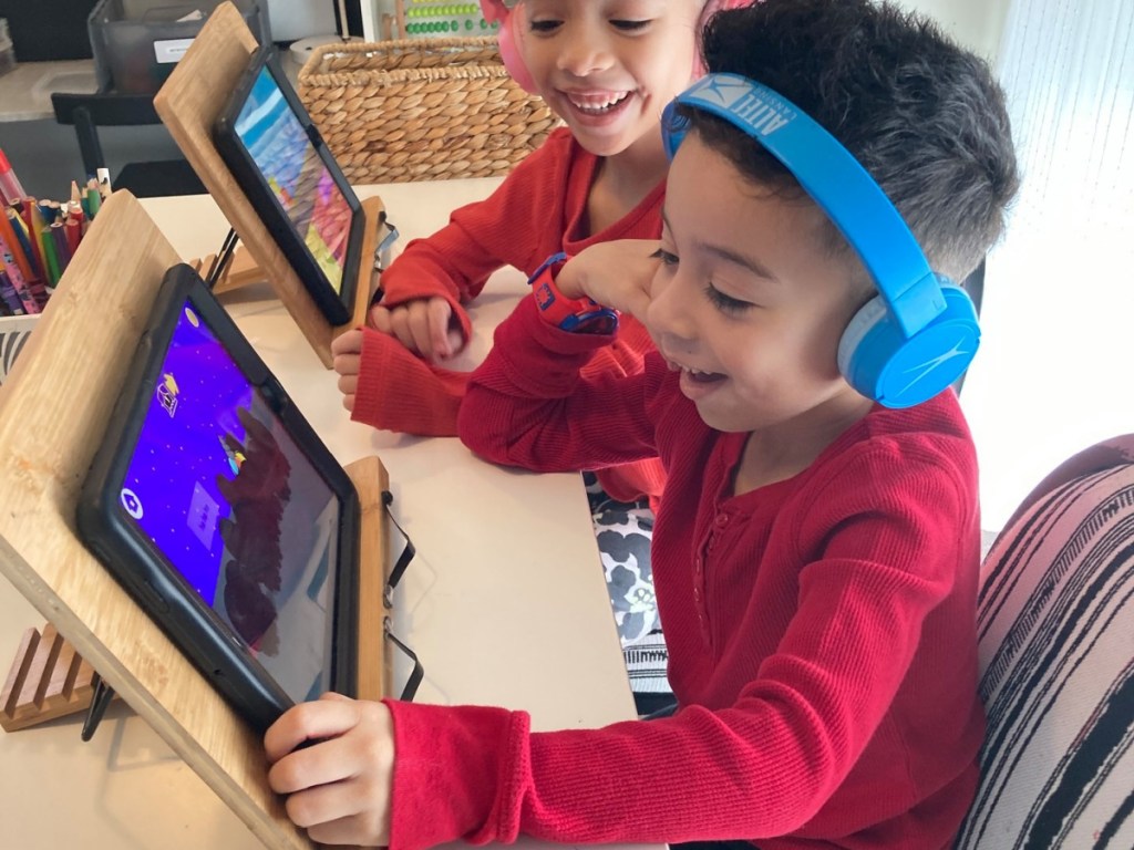two kids at home playing on tablets while smiling