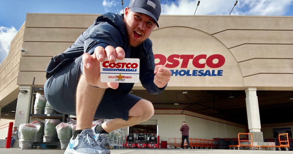 man holding a costco membership card in front of a Costco store