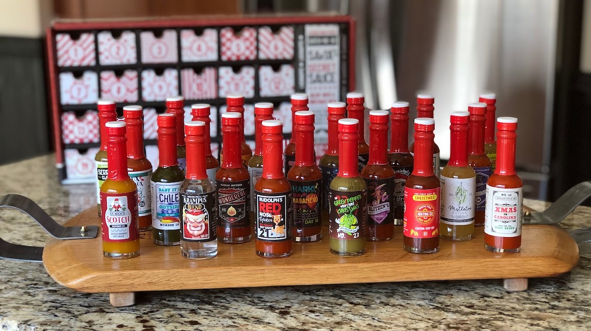 tons of hot sauces on wood table with advent calendar box in background