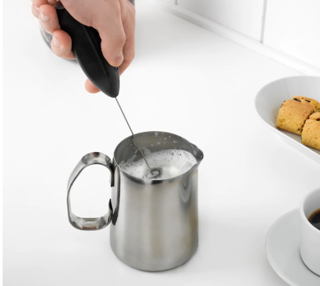 hand using ikea milk frother in stainless cup with milk