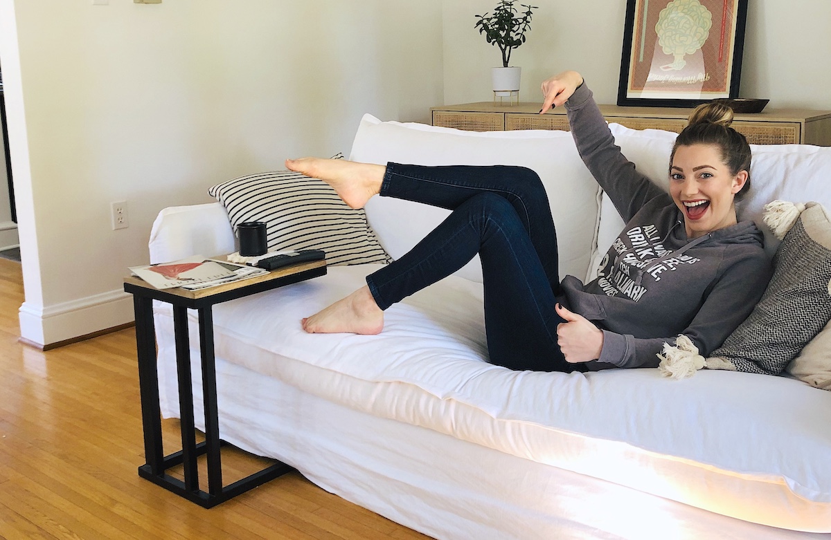 woman pointing to jeans with feet and legs in the air sitting on white couch