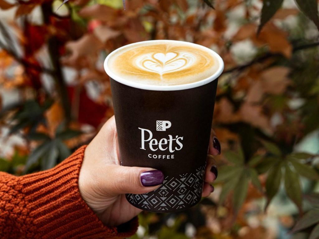 hand holding cup of coffee by fall leaves