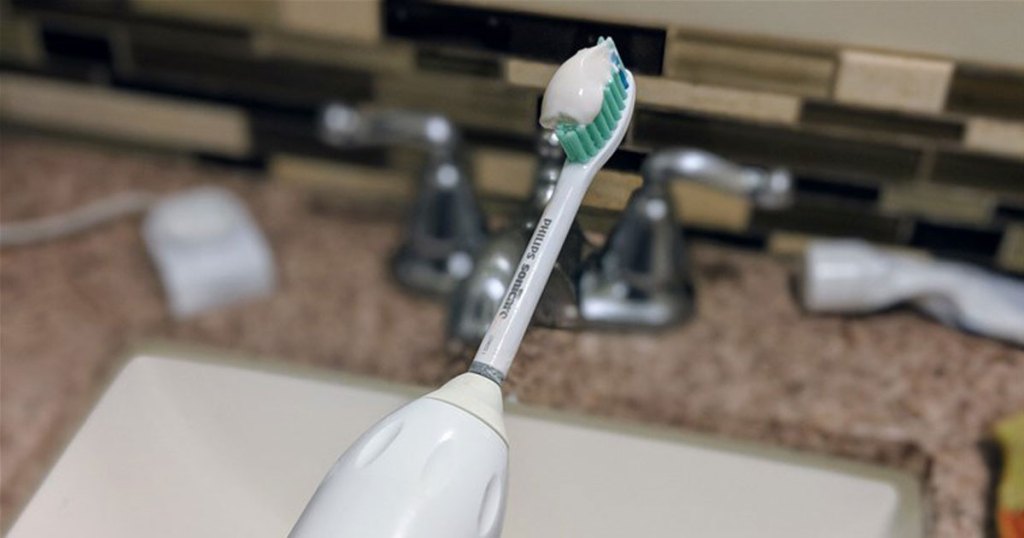 philips toothbrush with toothpaste on it and blurred bathroom sink in background