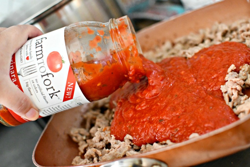 pouring marinara over ground meat in a skillet