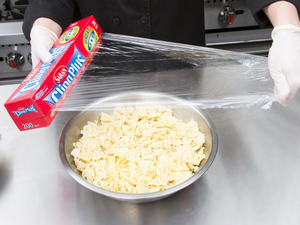 hands pulling out saran wrap to cover bowl of pasta
